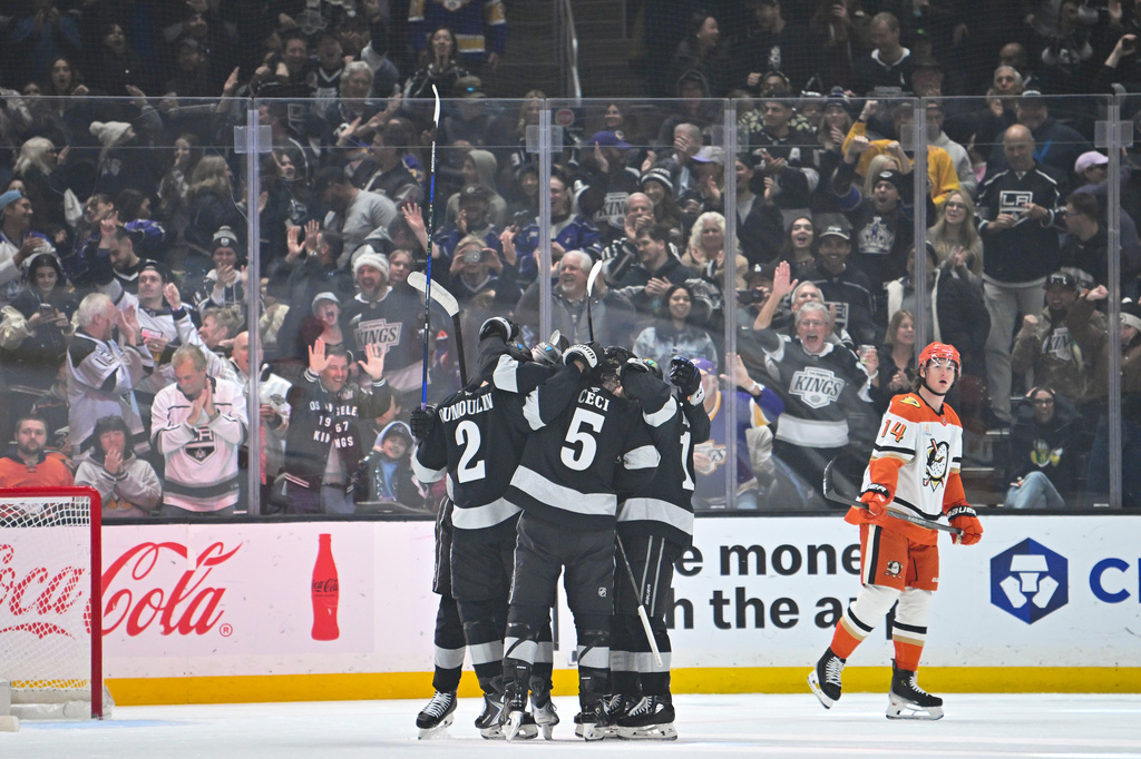 Los Angeles Kings left wing Trevor Moore (12), right, celebrates with Los Angeles Kings defenseman Brian Dumoulin (2), left, Los Angeles Kings defenseman Cody Ceci (5), center, and additional teammates after scoring a goal during the first period of an NHL hockey game against the Anaheim Ducks, Saturday, Dec. 27, 2025, in Los Angeles. (AP Photo/Katie Chin)