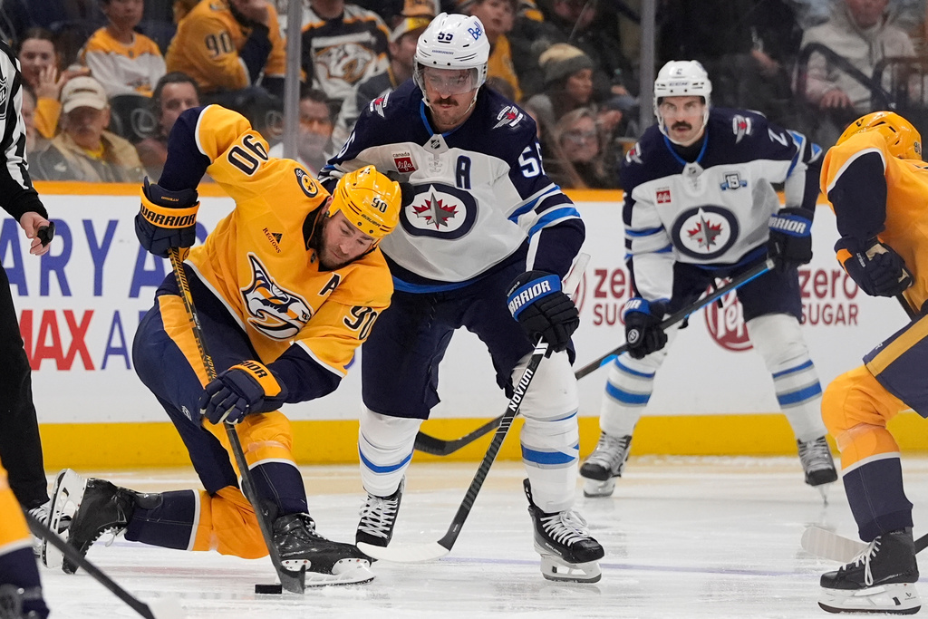 Nashville Predators center Ryan O'Reilly (90) hits the puck past Winnipeg Jets center Mark Scheifele (55) during the third period of an NHL hockey game Saturday, Nov. 29, 2025, in Nashville, Tenn. (AP Photo/George Walker IV)