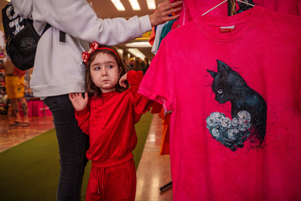 A child grimaces while looking at T-shirts displayed for sale at an international feline beauty competition, dubbed the Feline Oscars, featuring more than 200 cats, in Bucharest, Romania, Saturday, March 21, 2026. (AP Photo/Vadim Ghirda)