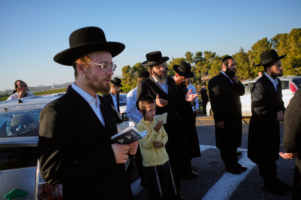 Ultra-Orthodox Jewish men and children pray on the roadside between Jerusalem and Tel Aviv during a protest against military conscription, Wednesday, June 24, 2026. (AP Photo/Ohad Zwigenberg)