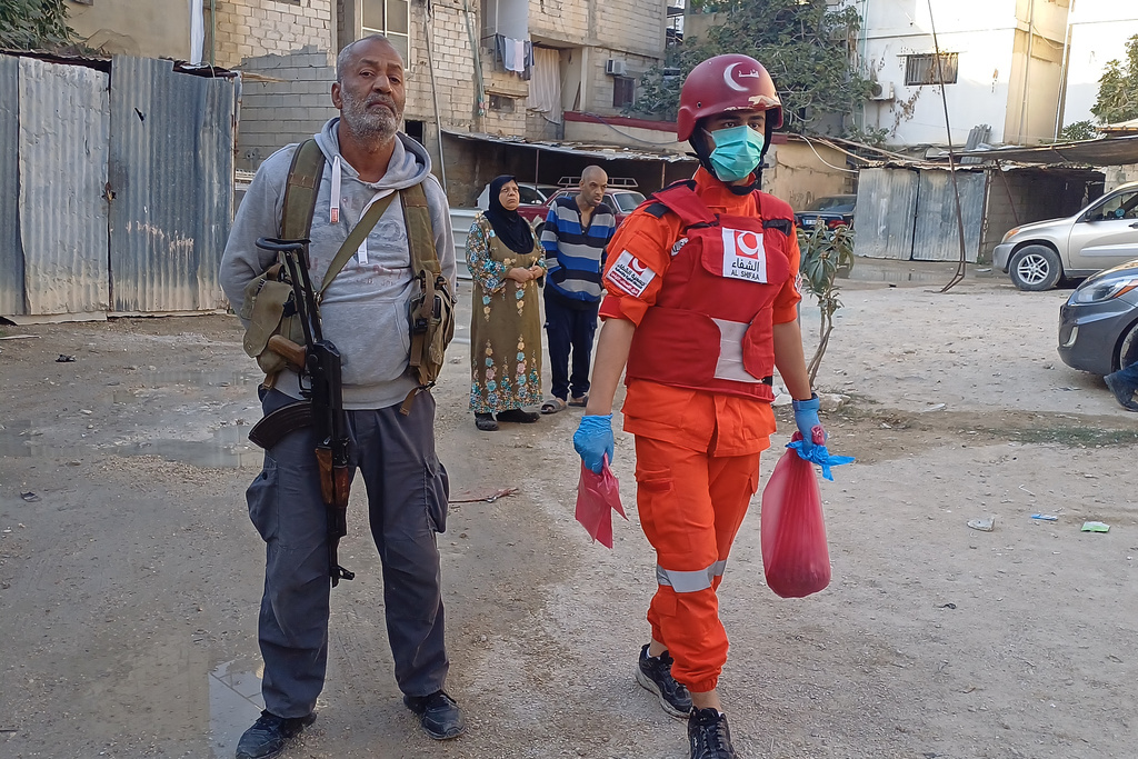 A Hamas gunman, left, stands next of a Palestinian rescue man who carries a bag with body remains, near the scene where an Israeli strike hit on Tuesday night the Ein el-Hilweh Palestinian refugee camp, in the southern port city of Sidon, Lebanon, Wednesday, Nov. 19, 2025. (AP Photo/Mohammed Zaatari)