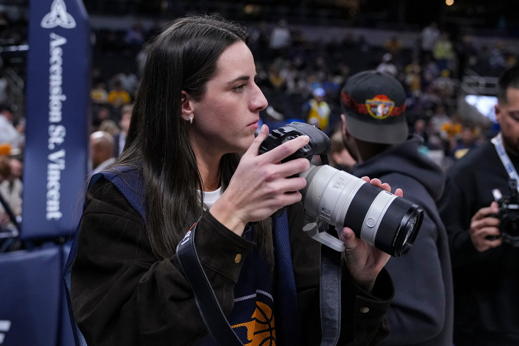 Indiana Fever guard Caitlyn Clark takes photos during pregame before an NBA basketball game between the Indiana Pacers and the Los Angeles Lakers in Indianapolis, Wednesday, March 25, 2026. (AP Photo/Michael Conroy)