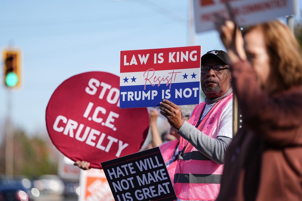 Protesters hold signs during the arrival of federal law enforcement, Wednesday, Nov. 19, 2025, in Charlotte, N.C. (AP Photo/Matt Kelley)
