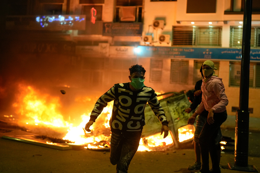 A person runs past a torched police vehicle as youth led protests calling for healthcare and education reforms turned violent, in Sale, Morocco, Wednesday, Oct. 1, 2025. (AP Photo/Mosa'ab Elshamy)