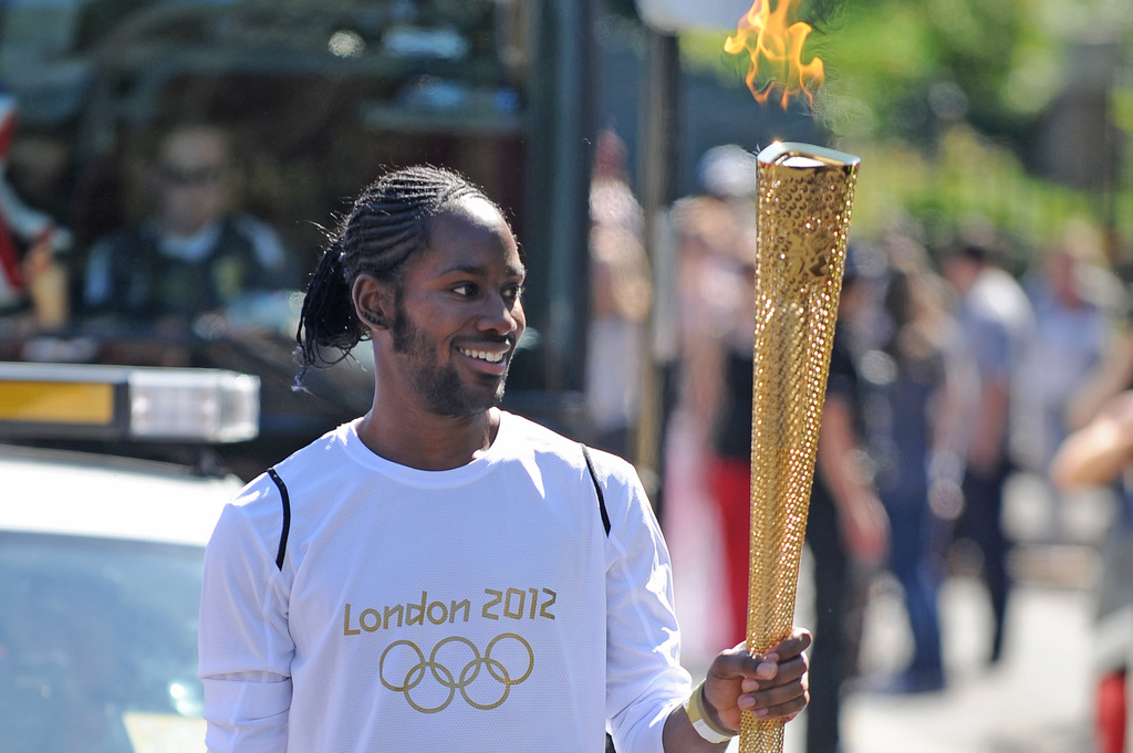 Torchbearer Jason Arday carries the Olympic Flame on the Torch Relay leg between Sutton and Merton, in London, July 23, 2012. (Joe Giddens/LOCOG/PA via AP)