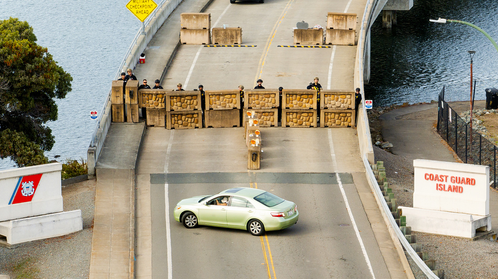 Coast Guardsmen stand watch behind a barrier at Coast Guard Base Alameda on Friday, Oct. 24, 2025, in Oakland, Calif. The barrier was erected earlier in the day after law enforcement officers fired on a vehicle as it backed towards them. (AP Photo/Noah Berger)