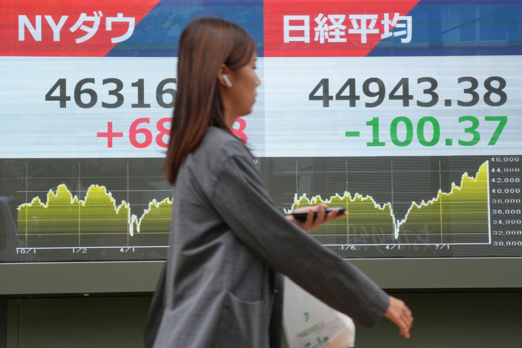 A person walks in front of an electronic stock board showing Japan's Nikkei 225 and New York Dow indexes at a securities firm Tuesday, Sept. 30, 2025, in Tokyo. (AP Photo/Eugene Hoshiko)