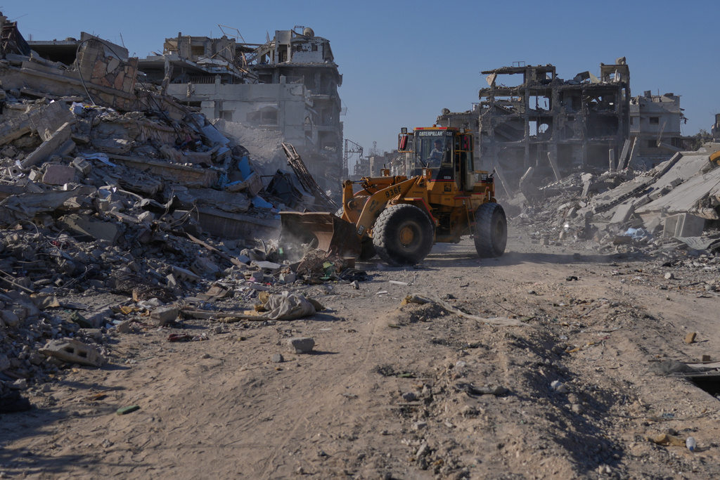 A Palestinian operates a mechanical shovel to clear a road surrounded by destroyed buildings in Khan Younis, in the southern Gaza Strip, Saturday, Oct. 11, 2025, after Israel and Hamas agreed to a pause in their war and the release of the remaining hostages. (AP Photo/Jehad Alshrafi)