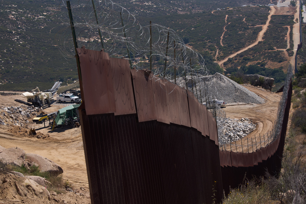Construction crews work on a new border wall segment near the end of a previously built section on Kuuchamaa Mountain, Friday, April 24, 2026, seen from Tecate, Mexico. (AP Photo/Gregory Bull)
