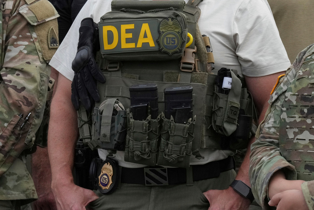 FILE - A Drug Enforcement Administration agent listens as President Donald Trump speaks with members of law enforcement and National Guard soldiers Aug. 21, 2025, in Washington. (AP Photo/Jacquelyn Martin, File)