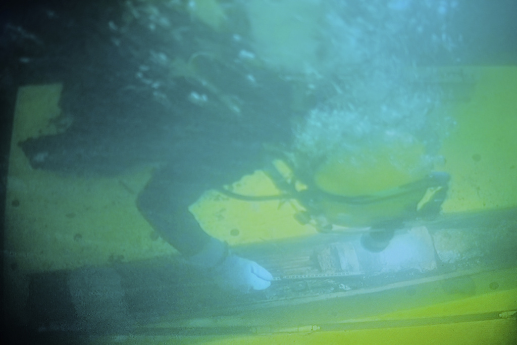 In this photo taken from a surveillance monitor, a diver works on a 128-millimeter artillery grenade during a press tour to show the recovering of ammunition from World War II in the Baltic Sea near Boltenhagen, Germany, Monday, Sept. 1, 2025. (AP Photo/Markus Schreiber)