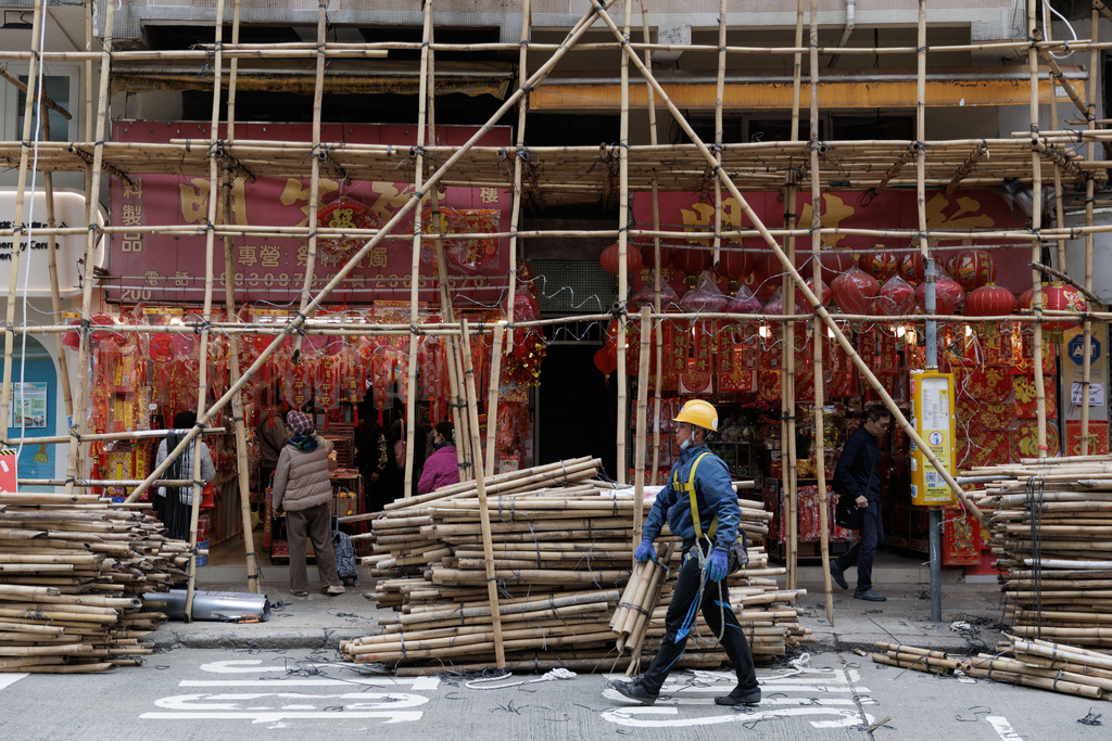 A worker walks past a shop selling Lunar New Year decorations beneath scaffolding in Hong Kong, Feb. 9, 2026. (AP Photo/May James)
