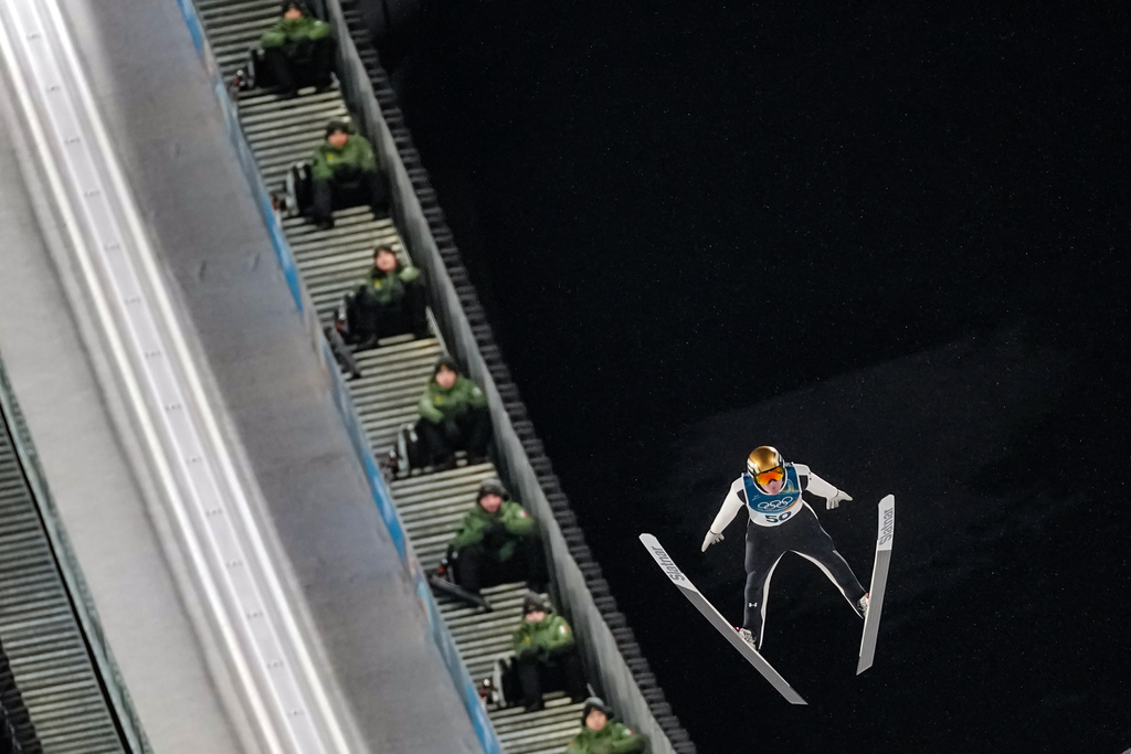 Italian Army soldiers on the steps of the ramp watch Domen Prevc, of Slovenia, soaring through the air during his first round jump of the ski jumping men's large hill individual at the 2026 Winter Olympics, in Predazzo, Italy, Saturday, Feb. 14, 2026. (AP Photo/Matthias Schrader)