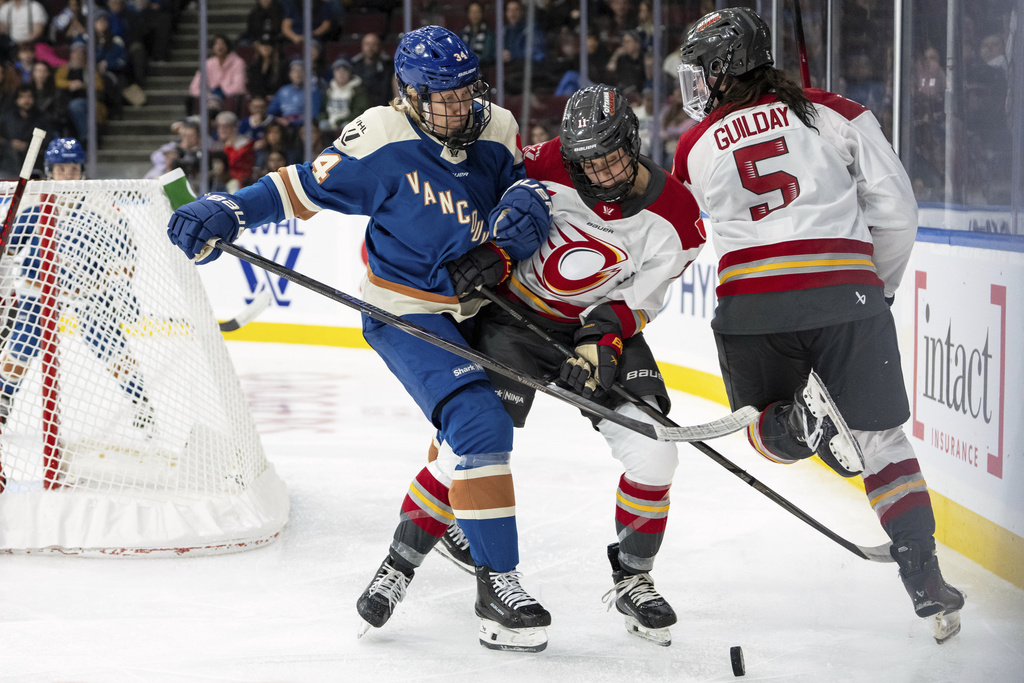 Vancouver Goldeneyes' Hannah Miller (34) hits Ottawa Charge's Brooke Hobson (11) as Rory Guilday (5) watches during the third period of a PWHL hockey game in Vancouver, British Columbia, Tuesday, Dec. 16, 2025. (Ethan Cairns/The Canadian Press via AP)