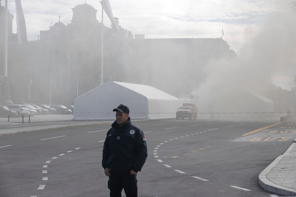 A policeman stands guard as a fire is localized inside the government supporters' camp outside the Serbian parliament in Belgrade, Serbia, Wednesday, Oct. 22, 2025. (AP Photo/Marko Drobnjakovic)
