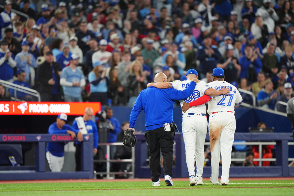 Toronto Blue Jays catcher Alejandro Kirk, right, and a team trainer, left, help pitcher Mason Fluharty leave the game after he was hit by a second come-backer in the seventh inning of a baseball game against the Athletics in Toronto, Saturday, March 28, 2026. (Frank Gunn/The Canadian Press via AP)