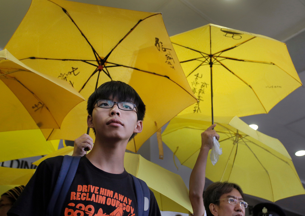 FILE - Hong Kong teenage student leader Joshua Wong, left, stands in front of yellow umbrellas outside a magistrates' court in Hong Kong, on Sept. 2, 2015. (AP Photo/Vincent Yu, File)