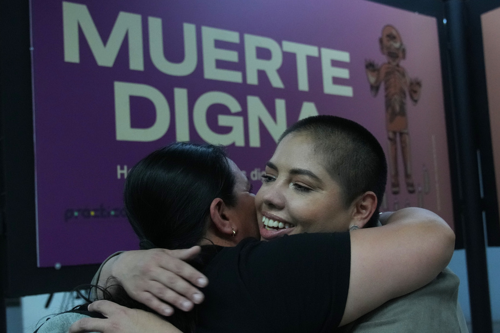 Samara Martínez, a supporter of a law to decriminalize euthanasia, hugs a friend during the "Muerte Digna," or Dignified Death, exhibition at the Ermita metro station in Mexico City, Monday, March 23, 2026. (AP Photo/Marco Ugarte)