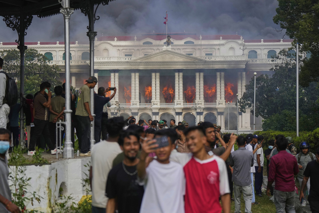 Protesters take selfies and celebrate at the Singha Durbar, the seat of Nepal's government's various ministries and offices, after it was set on fire during a protest against social media ban and corruption in Kathmandu, Nepal, Tuesday, Sept. 9, 2025. (AP Photo/Niranjan Shrestha)