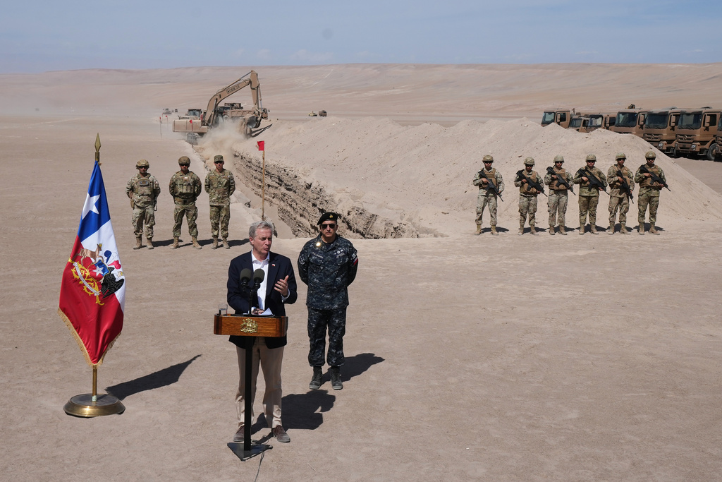 Chilean President Jose Antonio Kast gives a press conference as a machine digs, as part of measures to deter irregular migration, along the northern border at the Chacalluta border crossing, in Arica, Chile, Monday, March 16, 2026. (AP Photo/Esteban Felix)