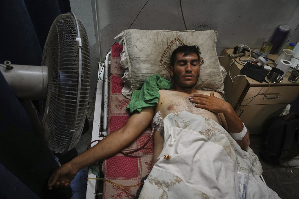 A Palestinian patient seeks relief from the heat by sitting near a fan during a heat wave, inside a warehouse set up in the yard of Shifa Hospital in Gaza City, Wednesday, Aug. 13, 2025. (AP Photo/Jehad Alshrafi)