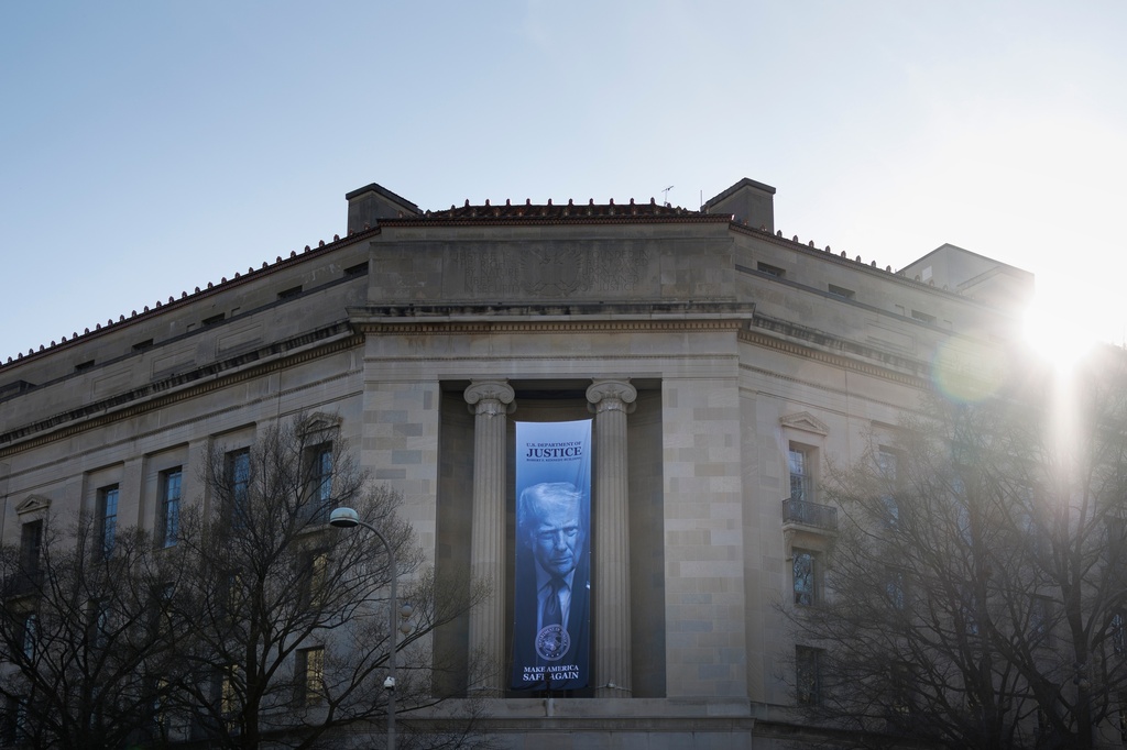 A banner of President Donald Trump hangs outside the U.S. Department of Justice on Saturday, March 21, 2026, in Washington. (AP Photo/Tom Brenner)