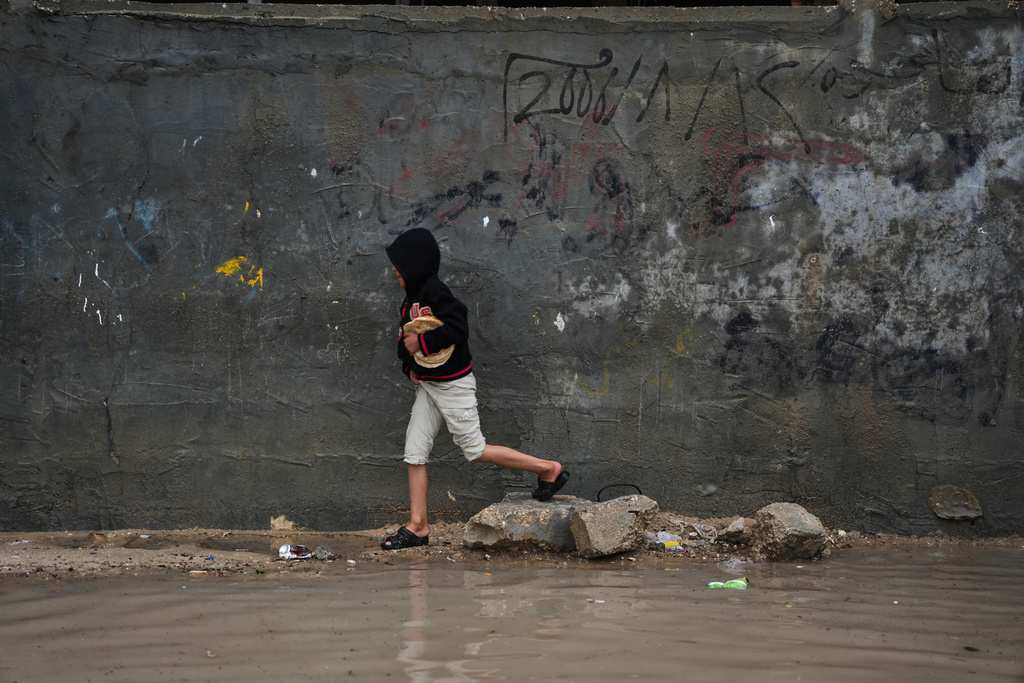 A displaced Palestinian child walks through a rain-soaked tent camp following heavy rainfall in Deir al-Balah, central Gaza Strip, Thursday, March, 26, 2026.(AP Photo/Abdel Kareem Hana)