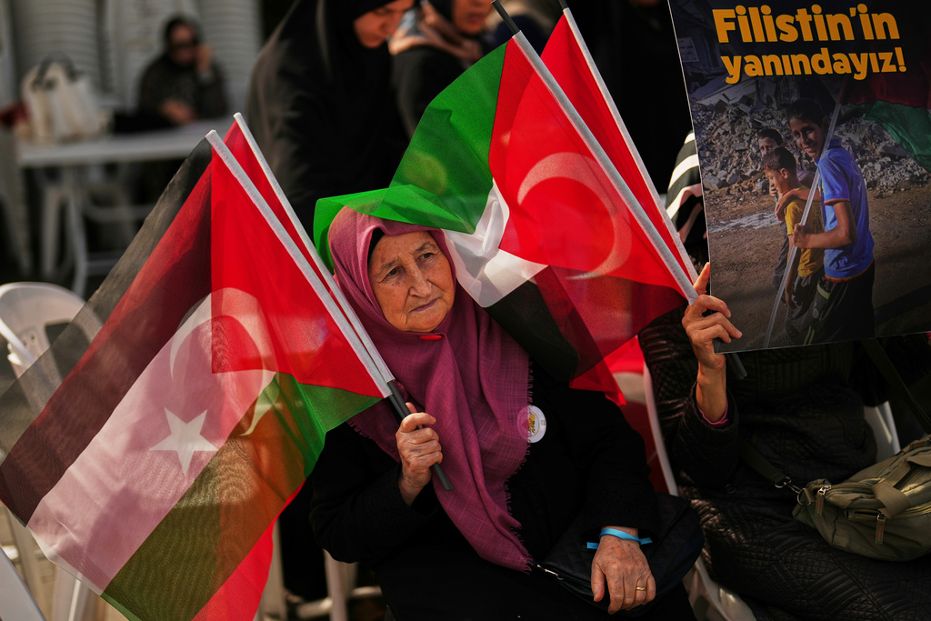 A woman waves Turkish and Palestinian flags during a sit-in gathering against the interception of the Gaza-bound Sumud flotilla by Israeli navy forces, in Istanbul, Thursday, Oct. 2, 2025. The board reads in Turkish: "We stand with Palestine". (AP Photo/Francisco Seco)