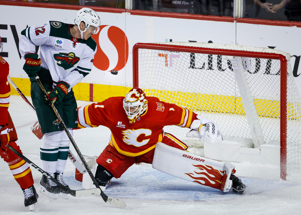 Minnesota Wild's Matt Boldy, second from right, jumps out of the way of the puck as Calgary Flames goalie Devin Cooley defends the net during the third period of an NHL hockey game in Calgary, Alberta, Thursday, Oct. 22, 2026. (Jeff McIntosh/The Canadian Press via AP)