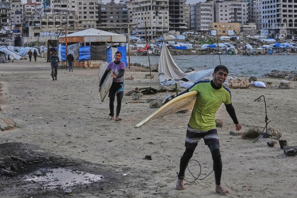 Palestinian Khalil Abu Jayyab, front, and Tahseen Abu Assi carry their surfing boards as they enter the water along a damaged shoreline in Gaza City, Sunday, Dec. 28, 2025. (AP Photo/Jehad Alshrafi)