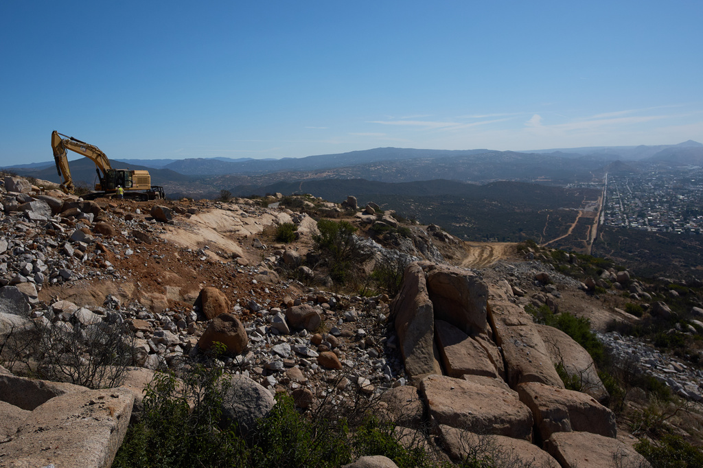 Construction crews work on a new border wall segment on Kuuchamaa Mountain, Friday, April 24, 2026, seen from Tecate, Mexico. (AP Photo/Gregory Bull)