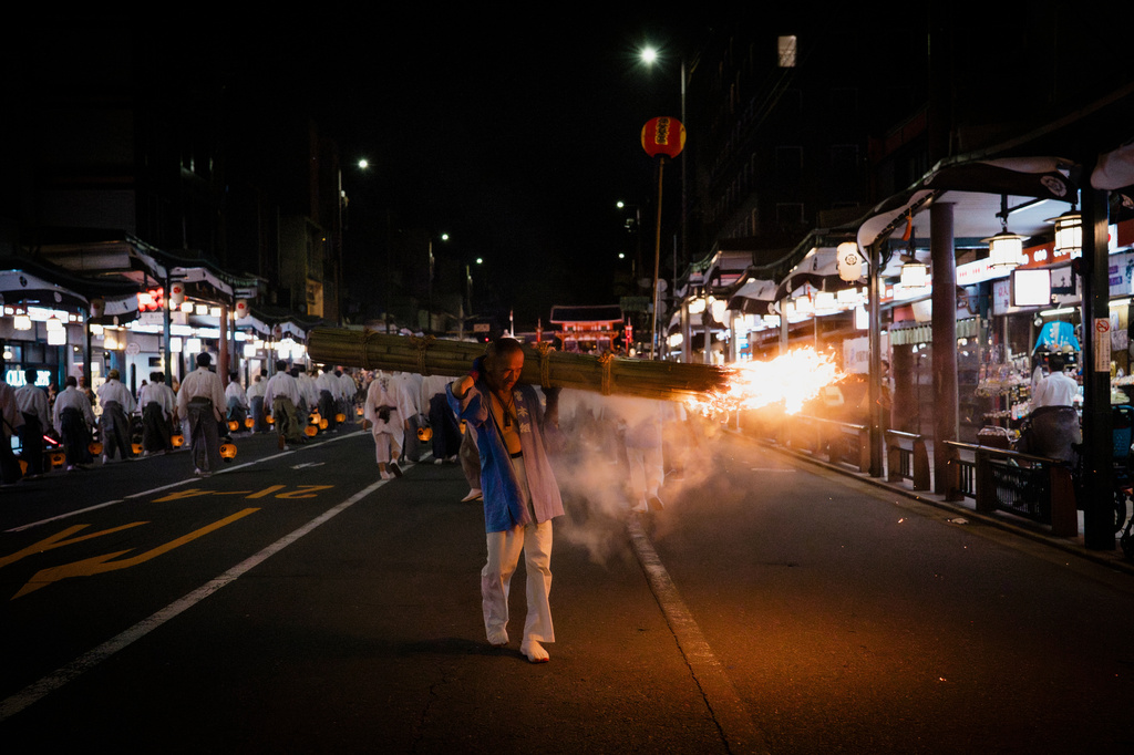 A festival participant carries a giant purification torch past tourists and local residents during the "Mikoshi Arai" purification ritual ahead of the Gion Matsuri festival in Kyoto, western Japan, Friday, July 10, 2026. (AP Photo/Fred Mery)