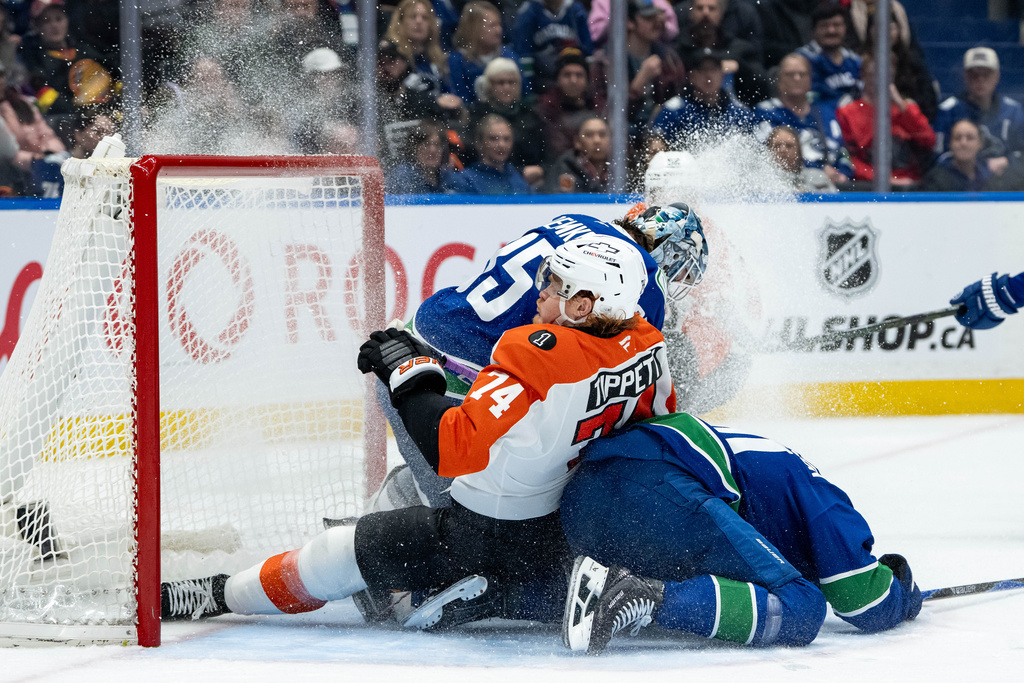Philadelphia Flyers' Owen Tippett (74) and Vancouver Canucks' Elias Pettersson, right, slide into goaltender Thatcher Demko (35) during the second period of an NHL hockey game in Vancouver, B.C., Tuesday, Dec. 30, 2025. (Ethan Cairns/The Canadian Press via AP)