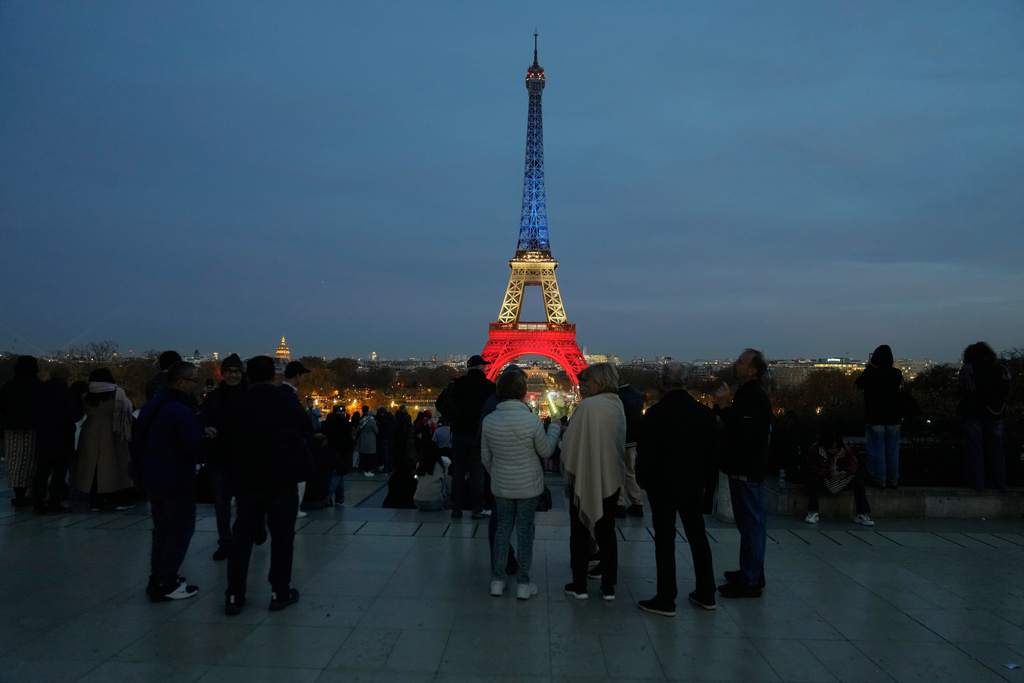 People gather at Trocadero Plaza as the Eiffel Tower is lit in the colors of the French national flag in Paris, Wednesday, Nov. 12, 2025, to honor the victims of the terror attacks at the Bataclan concert hall, cafes, and the national stadium 10 years ago. (AP Photo/Michel Euler)