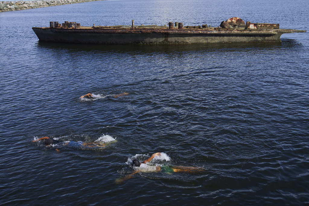 Children swim past the hull of a rusting boat at the port in Güiria, on Venezuela's Paria Peninsula, Saturday, Sept. 13, 2025. (AP Photo/Ariana Cubillos)