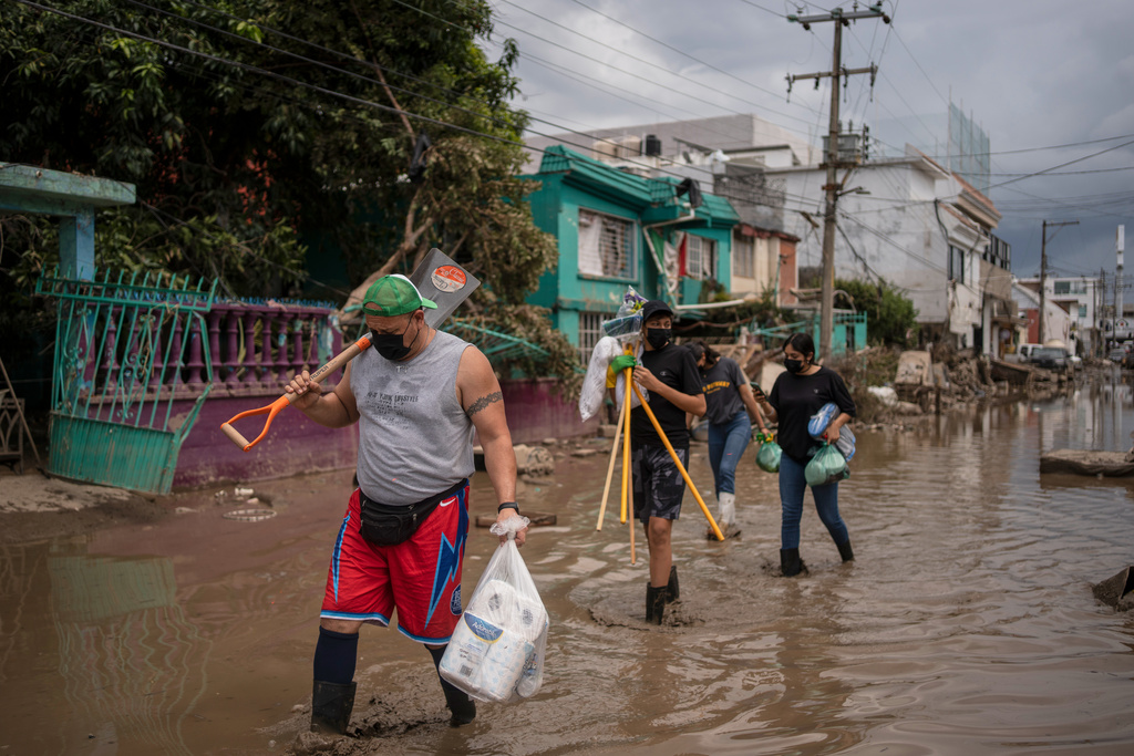 Locals transport supplies along a mud-covered street in Poza Rica, Veracruz state, Mexico, on Tuesday, Oct. 14, 2025, after landslides and torrential rain. (AP Photo/Felix Marquez)