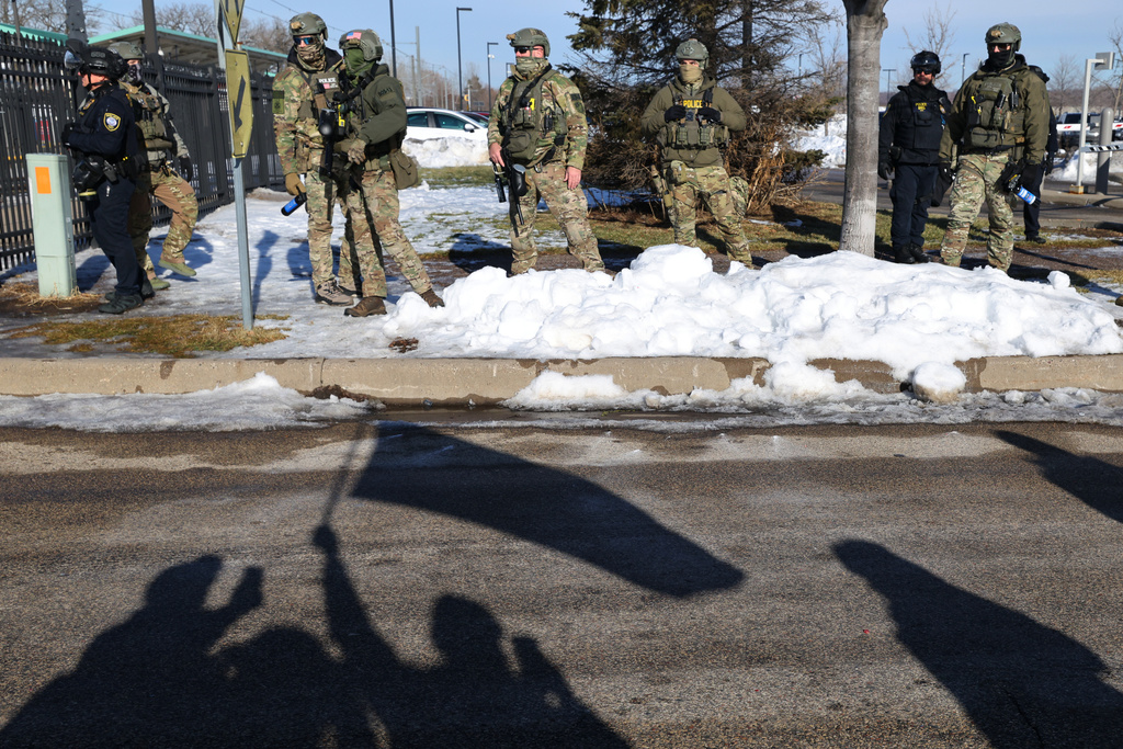Protesters' shadows are cast on the street near law enforcement outside the Bishop Henry Whipple Federal Building in Minneapolis, Friday, Jan. 9, 2026. (AP Photo/Adam Bettcher)