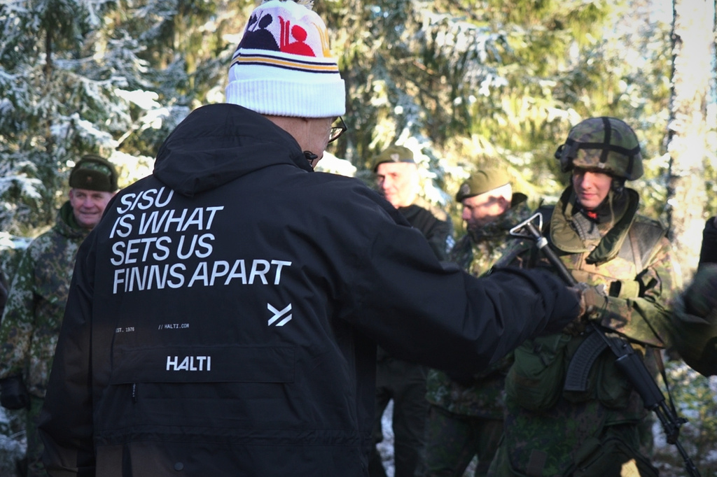 In this image from video, Finland's President Alexander Stubb greets Finnish defense volunteers taking part in training, while wearing a jacket that promotes the concept of "sisu" — resilience or endurance in Finnish — in Halvala, Finland, Saturday, Nov. 15, 2025. (AP Photo/Sergei Grits)