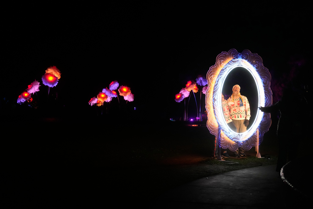 People have their photos taken in front of the San Francisco Botanical Garden's Peonies exhibit for Lightscape at Golden Gate Park in San Francisco, Wednesday, Dec. 17, 2025. (AP Photo/Jeff Chiu)