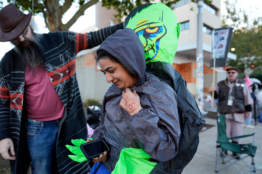 Brooks Brown, Operation Inflation co-founder, left, helps a demonstrator put on an inflatable costume outside a United States Immigration and Customs Enforcement (ICE) facility on Tuesday, Oct. 21, 2025, in Portland, Ore. (AP Photo/Jenny Kane)