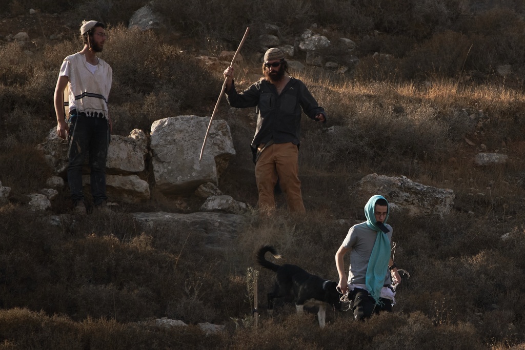 Israeli settlers walk down a hill as Israeli soldiers block access for Palestinians to an area for harvesting olives in the West Bank village of Sa'ir, near Hebron, Thursday, Oct. 23, 2025. (AP Photo/Leo Correa)