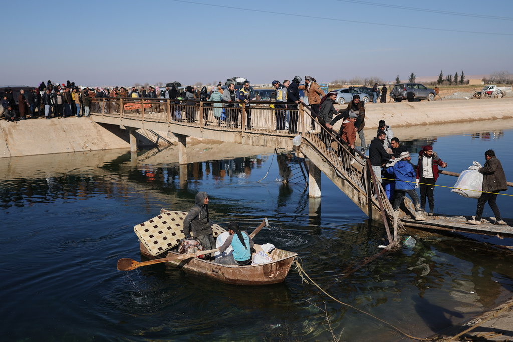 Displaced Syrians walk to cross at a river crossing near the village of Rasm al-Harmil al-Imam in the eastern Aleppo countryside, near the front line with the Kurdish-led Syrian Democratic Forces, in Deir Hafer, Syria, Friday, Jan. 16, 2026. (AP Photo/Ghaith Alsayed)