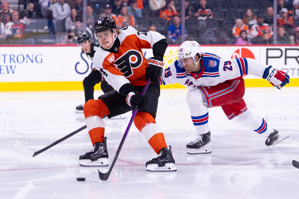 Philadelphia Flyers defenseman Nick Seeler, left, brings the puck into the zone with New York Rangers defenseman Matthew Robertson, right, trailing during the second period of an NHL hockey game, Monday, March 9, 2026, in Philadelphia. (AP Photo/Chris Szagola)