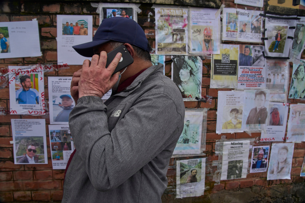 A man talks on his mobile phone after looking at photographs of people missing following flash floods displayed outside a government hospital in Kathmandu, Nepal, Tuesday, Sept. 1, 2026. (AP Photo/Niranjan Shrestha)