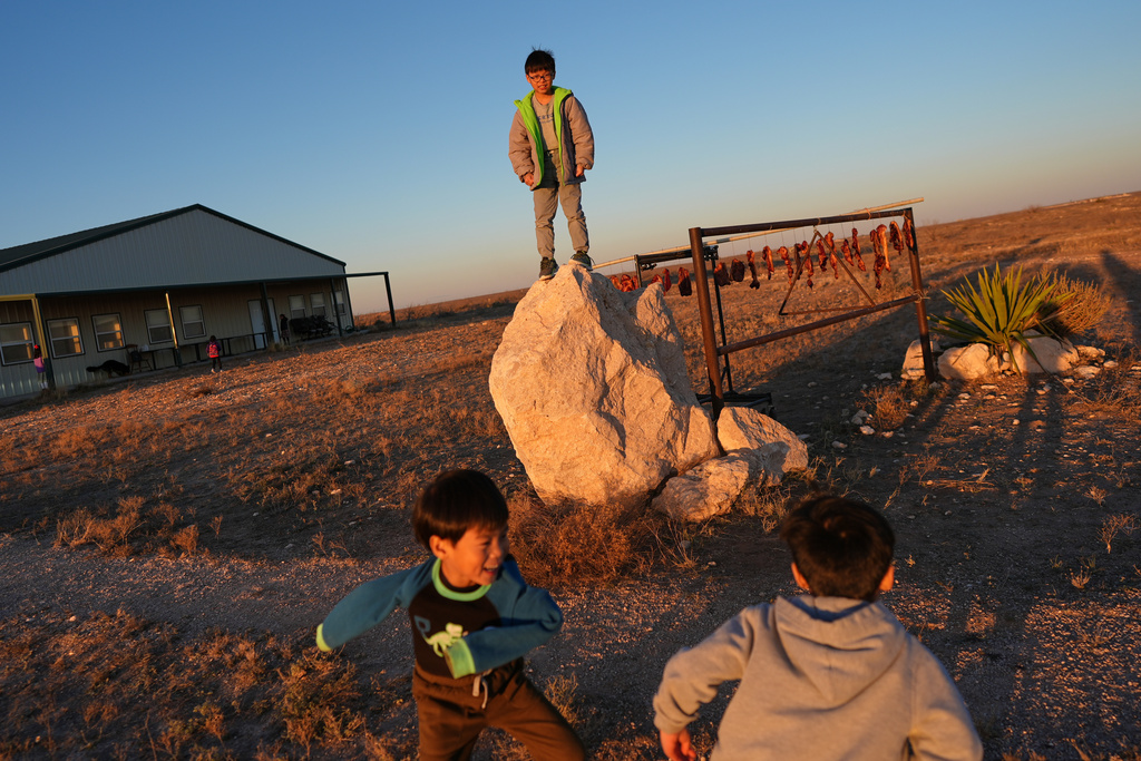 Young members of the Mayflower Church community play outside near pork belly strips curing on a pole to make a traditional Chinese bacon known as là ròu, in Midland, Texas, Jan. 18, 2025. (AP Photo/Rebecca Blackwell)