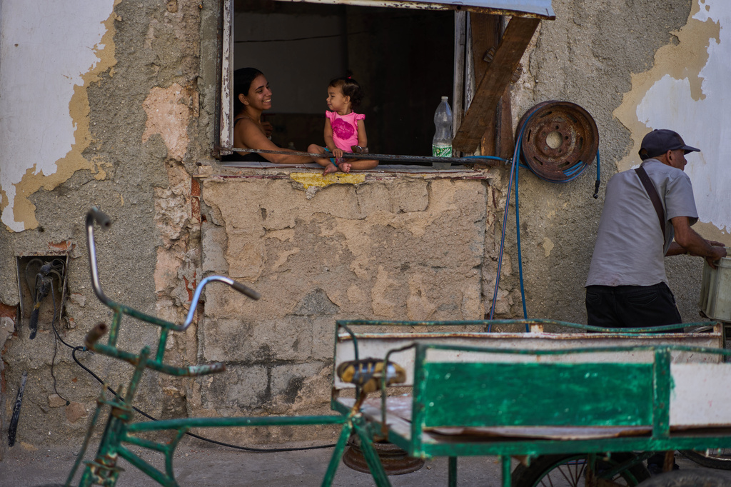 A child sits on a window ledge, chatting with an adult at a private bicycle wheel repair workshop in Havana, Cuba, Thursday, April 23, 2026. (AP Photo/Ramon Espinosa)