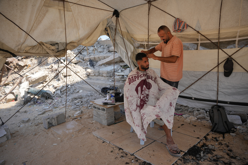 Palestinian barber Mousa al-Kharibi gives a man a haircut inside a tent, by the rubble of buildings that were destroyed during the Israel Hamas war, in Khan Younis, southern Gaza Strip, Friday, July 31, 2026. (AP Photo/Abdel Kareem Hana)