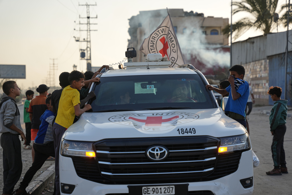 Palestinian kids look into a Red Cross vehicles carrying the bodies of two people believed to be deceased hostages handed over by Hamas make their way toward the Kissufim border crossing with Israel, to be transferred to Israeli authorities, in Deir al-Balah, central Gaza Strip, Thursday, Oct. 30, 2025. (AP Photo/Abdel Kareem Hana)