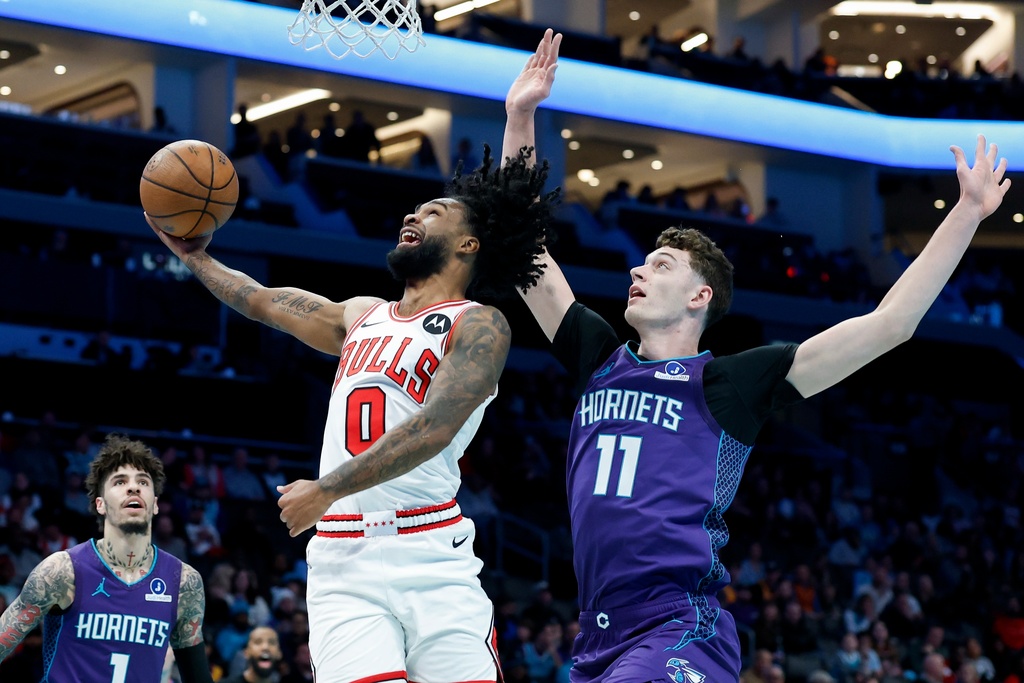 Chicago Bulls guard Coby White (0) drives to the basket against Charlotte Hornets center Ryan Kalkbrenner (11) as guard LaMelo Ball looks on during the first half of an NBA Cup basketball game in Charlotte, N.C., Friday, Nov. 28, 2025. (AP Photo/Nell Redmond)
