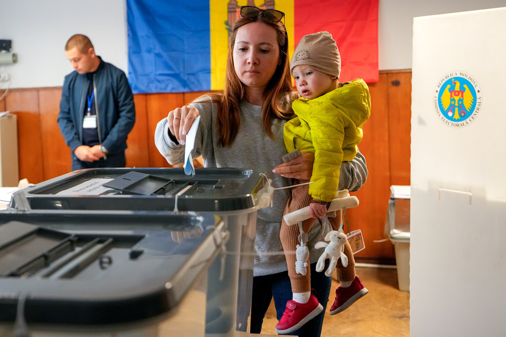 A woman holds a child as she casts her vote during a parliamentary election, in Chisinau, Moldova, Sunday, Sept. 28, 2025. (AP Photo/Vadim Ghirda)
